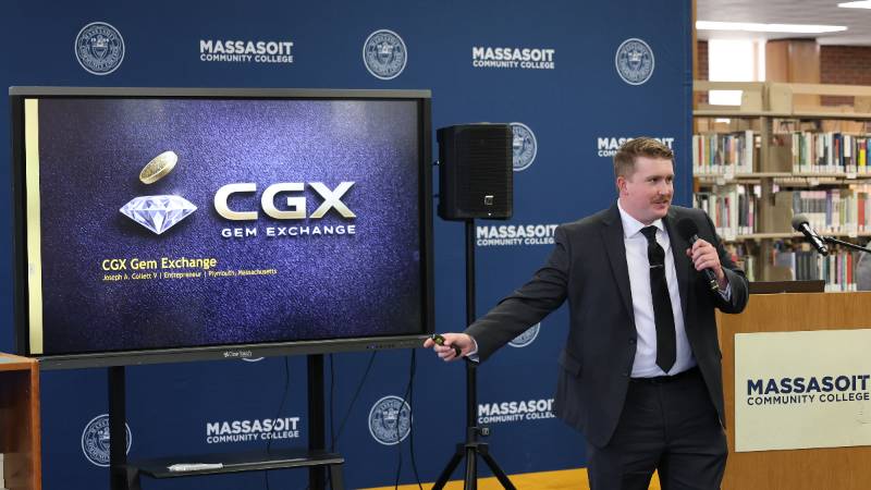 Joseph Collett standing in front of a screen with his business name at Massasoit's inaugural Entrepreneurship Challenge
