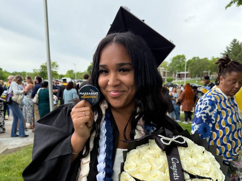 Graduate holding up a Massasoit Alumni blue button.